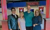 Four individuals are posing for a photo in a movie theater lobby, with two in casual attire flanked by two others dressed in more elaborate, performance-style outfits.