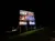 A nighttime photo of a lit-up roadside billboard advertising several entertainment acts, with a directional
