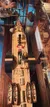 The image shows a model of a historic sailing ship, with its details reflected on a glossy surface, where several people appear to be captured in the reflection above the model.