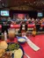 This image shows a meal consisting of green beans, mashed potatoes, a roll, and a meat dish, served on a blue plate at a table with ketchup and hot sauce, with a background of an audience seated at a dinner theatre watching a performance on a stage.