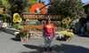 A person is standing in front of the Silver Dollar City sign, decorated with a rustic aesthetic and bright sunflowers, on a sunny day.