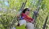 A person enjoys a ride on a swing carousel amid green foliage on a sunny day.
