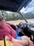A person is sitting in the driver's seat of an off-road vehicle, glancing at the camera, with outdoor surroundings visible through the windshield.