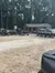 This is an image showing a group of people by a small building surrounded by several all-terrain vehicles in a clearing with trees in the background.