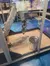 The image shows a robotic arm within a glass enclosure, positioned over a scattering of coins next to a metal pot on the floor, possibly part of an interactive exhibit or demonstration.