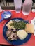The image shows a meal consisting of green beans, mashed potatoes, shredded meat, a bread roll, and a small bowl of gravy, accompanied by two glasses of water on a red table.