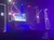 The image shows a brightly lit concert stage set up with vibrant stage lights, a large screen displaying graphics, and pillars with the letter 'R' outlined in light.