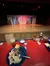 The image shows a partially eaten meal on a table with a clear view of a theater stage set with rustic barn doors in the background.