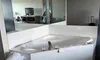 The image shows a hotel room with a large bathtub, mirror, and television, with a reflection of someone taking the photo.