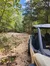 A side-by-side vehicle is parked on a rocky forest trail surrounded by early autumn foliage under a clear blue sky.