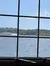 A clear day's view through a window pane with spots and streaks, overlooking a body of water with trees and buildings in the distance.
