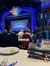 The image shows an audience seated at dining tables inside a theater, waiting for a performance to begin at the