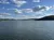 The image shows a tranquil expansive lake with hills in the background under a partly cloudy sky.