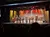 A band of musicians is performing on stage in front of an audience, illuminated by colorful stage lighting.