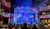 A lively musical performance is underway on a patriotically-themed stage with an audience in the foreground enjoying the show.