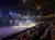 The image depicts an indoor equestrian performance, with riders in colorful costumes entertaining an audience in a dimly lit arena, accompanied by dramatic lighting and effects that simulate a starry atmosphere.