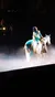 A performer in an elaborate costume rides a white horse on a foggy stage, possibly during a theatrical show or equestrian performance.