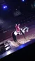A performer on a black and white horse is applauding the audience in an indoor arena with onlooking spectators.