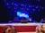 The image shows an auditorium with a stage set for a performance, featuring musical instruments and a large screen displaying