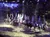 A group of cowboys on horseback perform under falling snowflakes in a festive, illuminated arena.