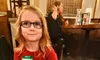 A child with glasses sits at a table in a restaurant with a plate of ravioli, meatballs, green beans, and a dessert.