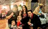 A group of people, including adults and children, are posing cheerfully in a brick-walled, restaurant-like setting with a performer.