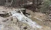 A small waterfall flows over rocky terrain surrounded by a forest with bare trees.