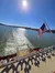 The image shows a sunny day over a body of water viewed from a boat with an American flag, leaving a trail in the water.