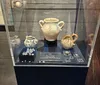 The image shows a display case containing three ceramic jugs and an assortment of beads, with descriptions indicating the types of beads.