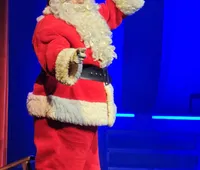 A person dressed as Santa Claus is waving on stage against a blue backdrop.