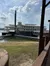 A large paddlewheel riverboat is docked by a grassy shore under a partly cloudy sky.