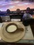 A bowl of creamy soup and a drink are placed on a table in a venue overlooking a live performance arena with an audience.