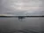 A small, tree-covered island sits in the middle of a calm lake under a cloudy sky with distant hills on the horizon.