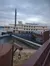 A large riverboat with multiple decks and a tall smokestack is docked near a pier, under a cloudy sky.