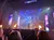 A stage performance features a helicopter with vibrant lighting and controlled fire effects, viewed by an audience.