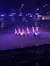 Performers on horseback, carrying American flags, are on an indoor arena stage, illuminated by dramatic lighting, with spectators in the background.