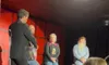 A group of people are on stage in a dimly lit room, possibly participating in an event or performance.
