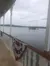 The image shows a view of a lake with a small island in the distance, seen from a boat deck adorned with a decorative red, white, and blue banner.