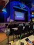 Audience members are seated at tables in a theater, facing the stage displaying a