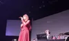 A woman in a red dress is singing on stage with a band accompanying her.