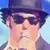 A person wearing a suit, hat, and sunglasses is performing on stage with a microphone.