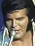 A performer dressed in a white jumpsuit is singing on stage with a band in the background.