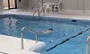 A person is swimming in an indoor pool with a white poolside chair and table nearby.