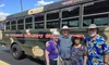 A group of four people, dressed casually and smiling, stands in front of a bus labeled