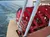 The image shows a red paddle wheel of a steamboat on a body of water with a backdrop of hills and a partly cloudy sky.