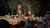A nighttime outdoor performance features riders on horses holding torches in front of an audience.