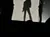 A silhouetted figure, wearing a hat, poses dramatically behind a backlit sheet held up by two people.