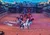 The image shows a live horse performance in an arena with riders wearing colorful costumes, flags, and a backdrop of a scenic landscape.