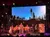 A group of musicians is performing on stage, set against a backdrop of a starry night sky with silhouetted trees.