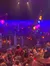 A crowded theater features a colorful and elaborate stage set with hanging lanterns, resembling a vibrant marketplace scene.